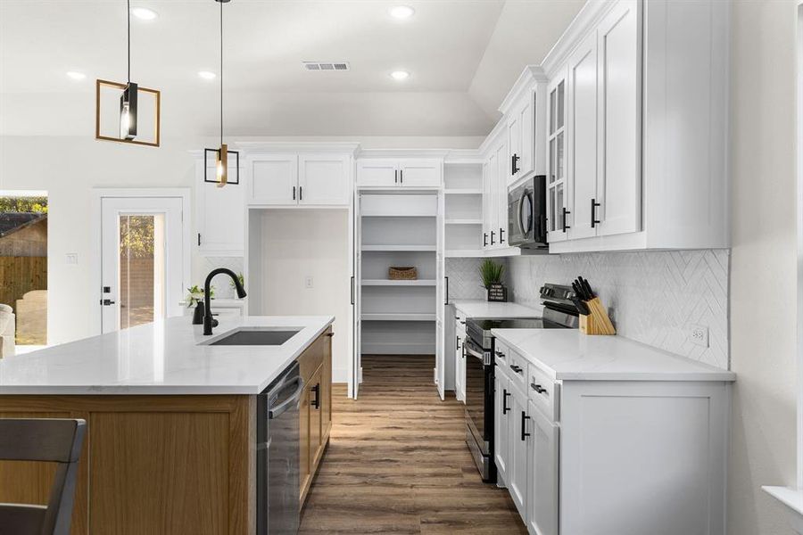 Kitchen with light stone countertops, white cabinets, decorative light fixtures, and appliances with stainless steel finishes