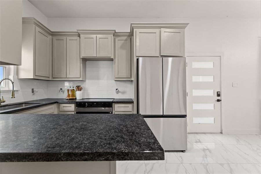 Contemporary kitchen featuring dark countertops, light gray cabinetry, stainless steel appliances, and a white subway tile backsplash Contemporary kitchen featuring dark countertops, light gray cabinetry, stainless steel appliances, and a white subway tile backsplash