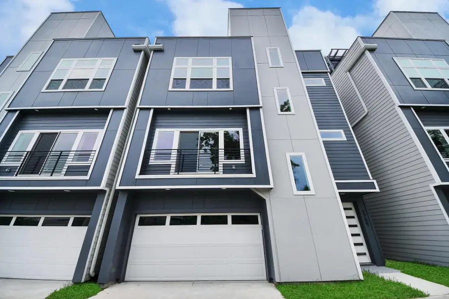 Modern four-story townhouse with a sleek facade, featuring large windows, a small balcony, and a two-car garage. The exterior is a combination of gray siding and panels, with a touch of green lawn in the front. Modern four-story townhouse with a sleek facade, featuring large windows, a small balcony, and a two-car garage. The exterior is a combination of gray siding and panels, with a touch of green lawn in the front.