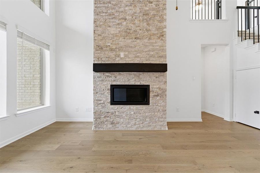 Two-story living area featuring a stacked stone fireplace with a dark wood mantel and a black firebox