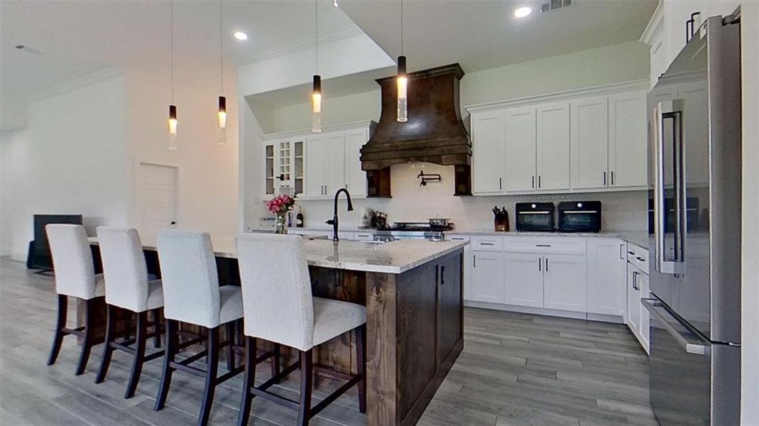 Spacious kitchen featuring a large island with seating, white cabinetry, integrated stainless steel appliances, a dark wood range hood, and tile flooring Spacious kitchen featuring a large island with seating, white cabinetry, integrated stainless steel appliances, a dark wood range hood, and tile flooring