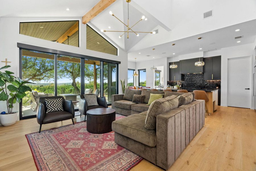 Open-concept living space with vaulted ceilings featuring exposed wood beams and light wood-finish flooring