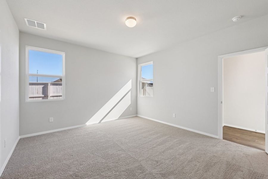 Image of a bedroom with light grey walls, tan carpeting and windows with white trim