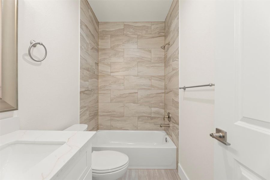 This bathroom features a modern design with a white vanity, a sleek countertop, and a bathtub surrounded by textured stone tile. Neutral tones create a bright and clean atmosphere.