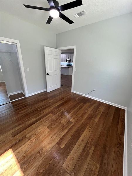 Unfurnished bedroom with dark wood-style floors, a textured ceiling, a ceiling fan, and a walk in closet Unfurnished bedroom with dark wood-style floors, a textured ceiling, a ceiling fan, and a walk in closet
