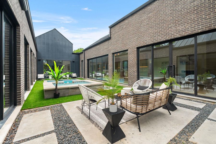Private courtyard featuring a plunge pool, synthetic turf lawn, concrete pavers with dark aggregate, and extensive sliding glass doors