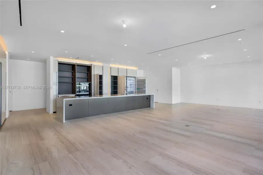 Kitchen featuring an expansive center island with sleek cabinetry, integrated open shelving, recessed ceiling lighting, and continuous wood-finish flooring