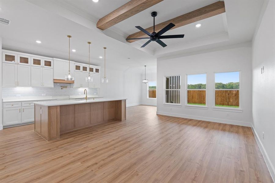 Kitchen with light countertops, light wood-type flooring, decorative backsplash, a sink, and beam ceiling