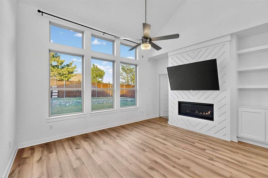 Unfurnished living room with a large fireplace, light wood finished floors, and a ceiling fan Unfurnished living room with a large fireplace, light wood finished floors, and a ceiling fan