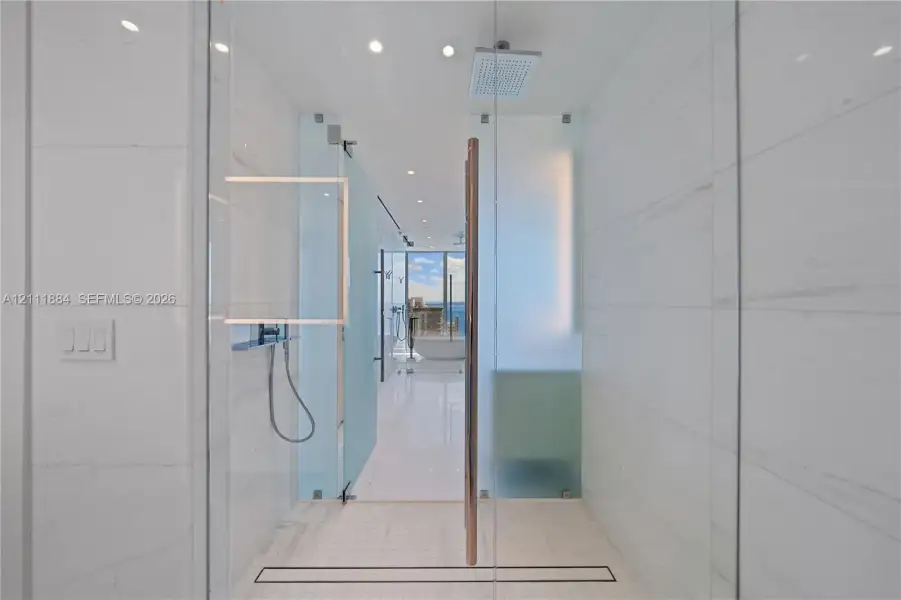 Walk-in shower featuring floor-to-ceiling tiled walls, frameless glass door, ceiling-mounted rainfall showerhead, handheld shower fixture, and linear drain Walk-in shower featuring floor-to-ceiling tiled walls, frameless glass door, ceiling-mounted rainfall showerhead, handheld shower fixture, and linear drain