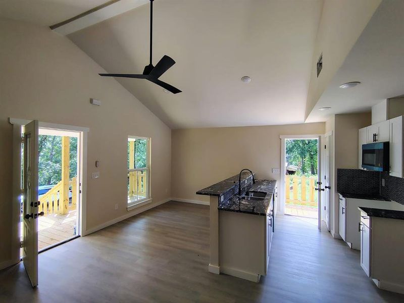 Kitchen featuring stainless steel microwave, ceiling fan, high vaulted ceiling, white cabinets, and wood finished floors