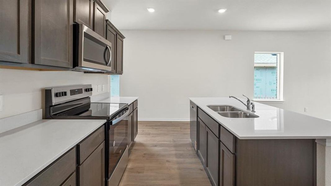 Contemporary kitchen featuring dark wood cabinetry, white countertops, stainless steel appliances, and wood-finish flooring