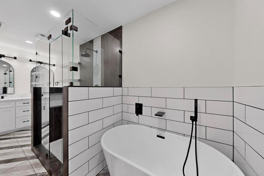 Bathroom with vanity, a freestanding tub, a tile shower, tile walls, and recessed lighting