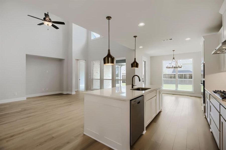 Open-concept kitchen and living area featuring a large center island with a built-in sink, pendant lighting, wood-finish flooring, and high ceilings