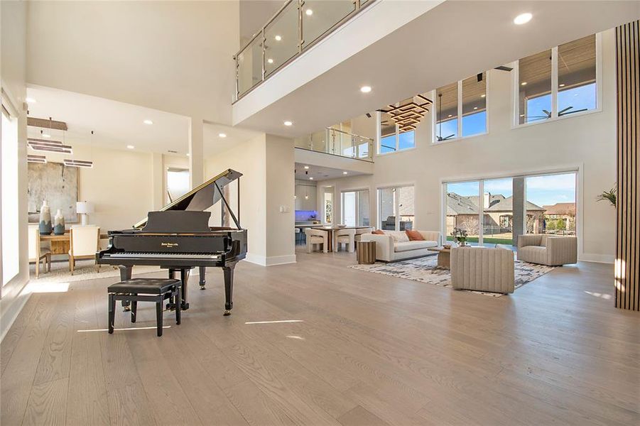 Living area featuring light wood-style floors, a towering ceiling, and recessed lighting Living area featuring light wood-style floors, a towering ceiling, and recessed lighting