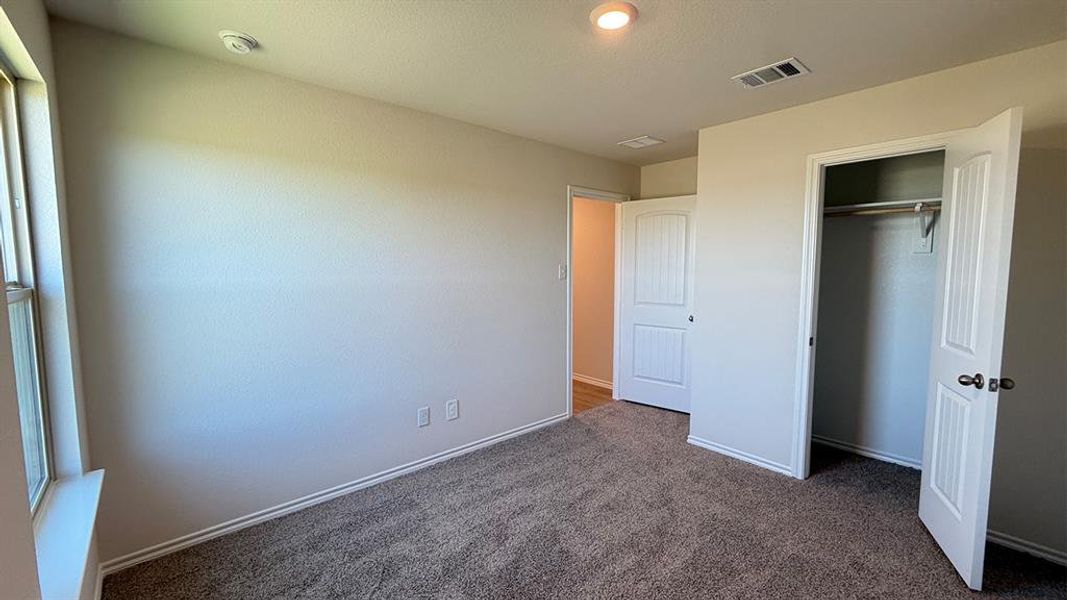 Neutral-toned bedroom featuring plush carpet flooring, a window with a sill, and a built-in closet with bi-fold doors and overhead shelving
