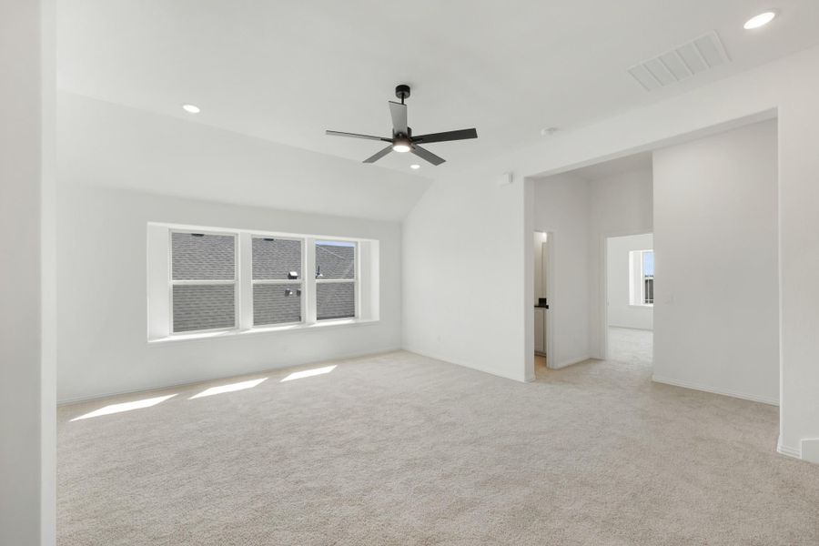 Empty bedroom with vaulted ceiling, black ceiling fan, carpet flooring, and triple windows