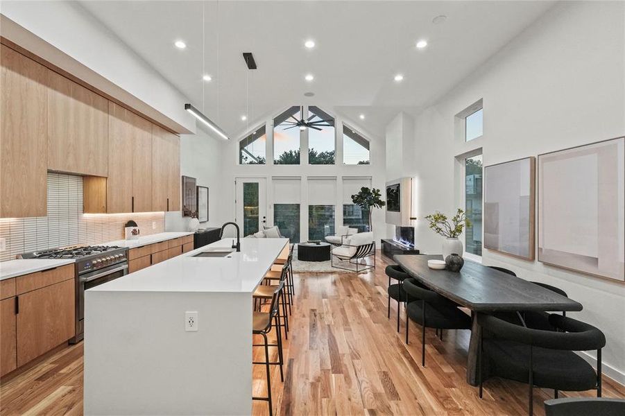 Kitchen with light hardwood / wood-style flooring, high end range, an island with sink, high vaulted ceiling, and a breakfast bar