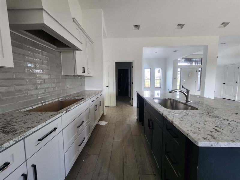 Kitchen featuring white shaker cabinetry, an expansive island with a stainless steel undermount sink, granite countertops, and wood-finish flooring