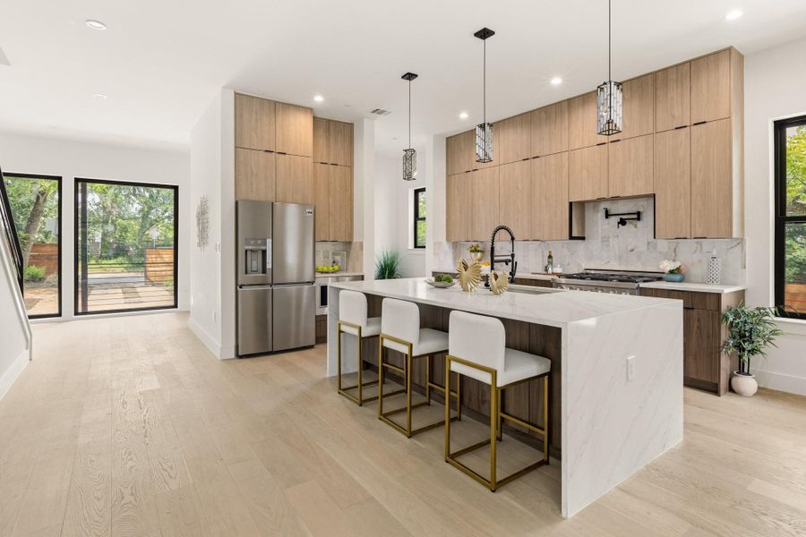 Gourmet kitchen with a waterfall island, wood-finish cabinetry, stainless steel appliances, and a marble-patterned backsplash