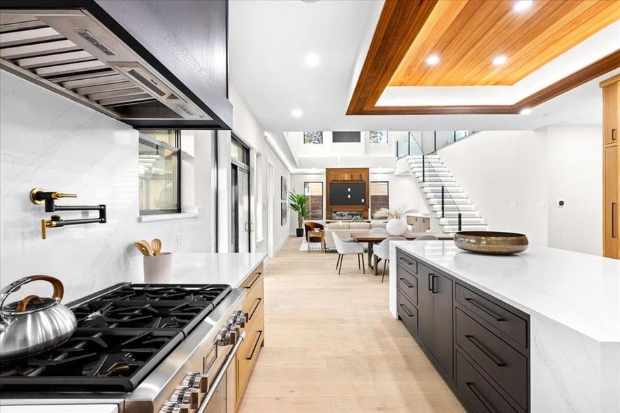 Kitchen with range with two ovens, light wood-type flooring, light stone countertops, a center island, and a tray ceiling