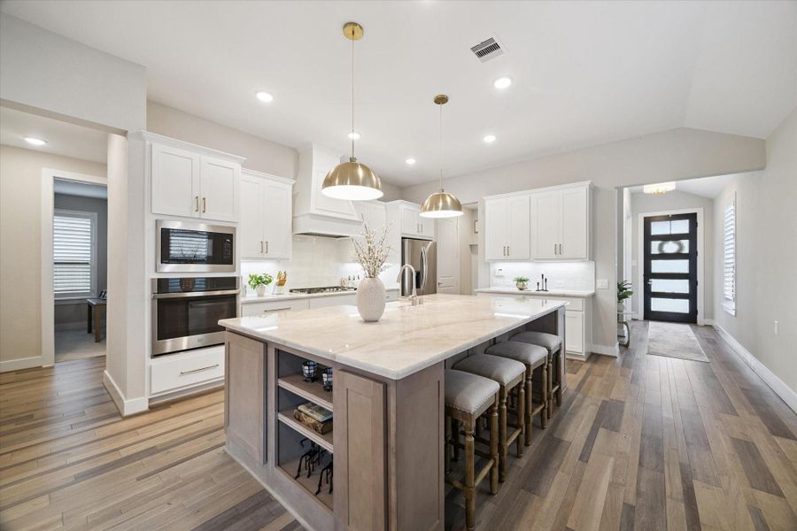 A designer kitchen anchored by a large Taj Mahal quartzite island with seating, pendant lighting, and soft-close cabinetry creates a true centerpiece for the home.
