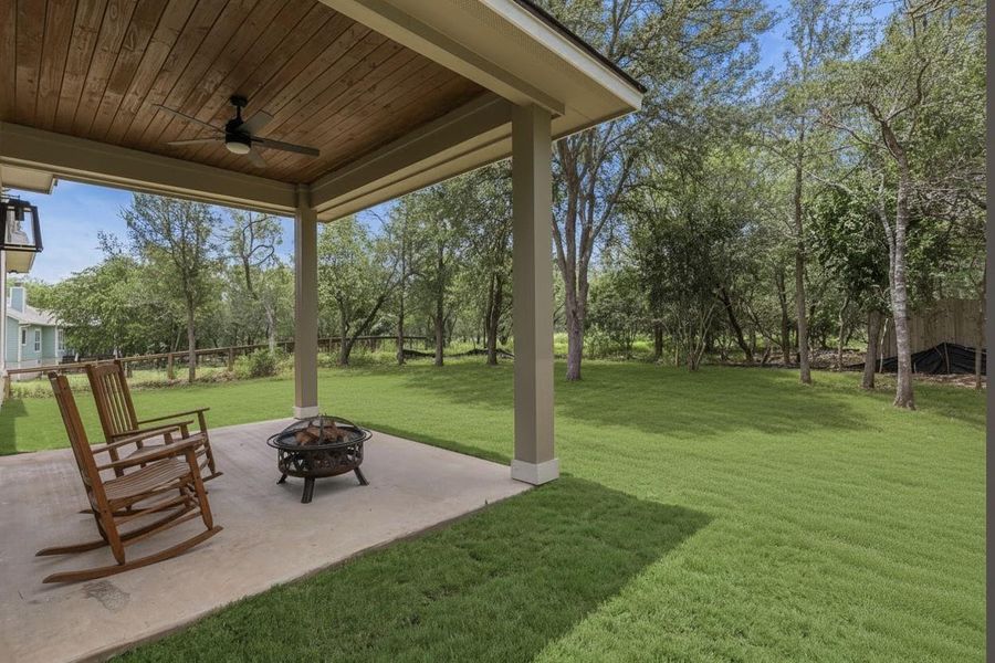An inviting covered patio featuring a wood plank ceiling and a fire pit, overlooking a lush, verdant yard.