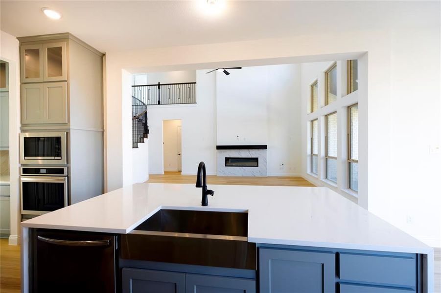 Kitchen featuring light stone countertops, stainless steel appliances, light wood-type flooring, a fireplace, and glass insert cabinets Kitchen featuring light stone countertops, stainless steel appliances, light wood-type flooring, a fireplace, and glass insert cabinets