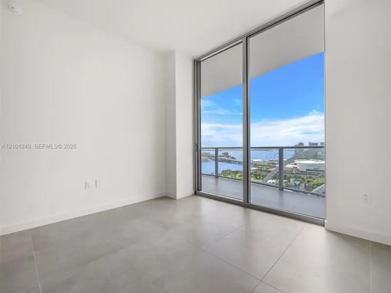 Floor-to-ceiling sliding glass doors, private balcony with metal and glass railing, large-format tile flooring, and water backdrop Floor-to-ceiling sliding glass doors, private balcony with metal and glass railing, large-format tile flooring, and water backdrop