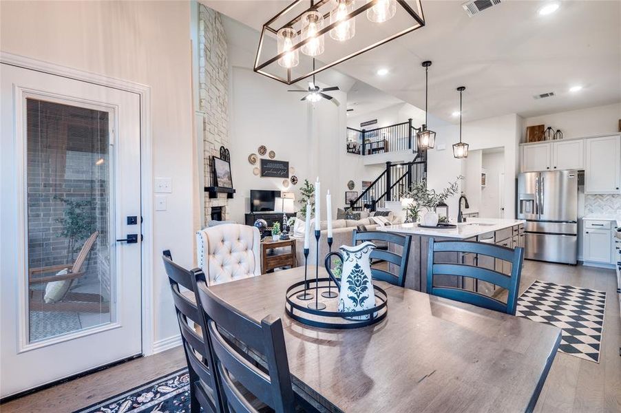 Dining room featuring stairs, a ceiling fan, dark wood-type flooring, a stone fireplace, and a high ceiling