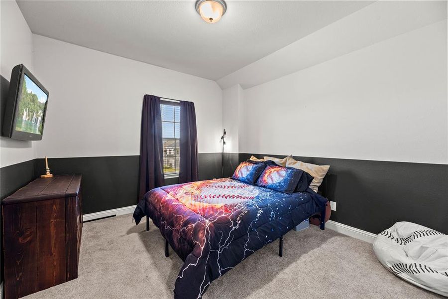 This is a cozy, well-lit bedroom featuring a two-tone wall with a dark lower half and light upper half, plush carpeting, a large window and a ceiling light fixture.