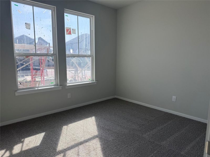 Double hung windows illuminate a carpeted secondary bedroom featuring clean lines and modern baseboards.