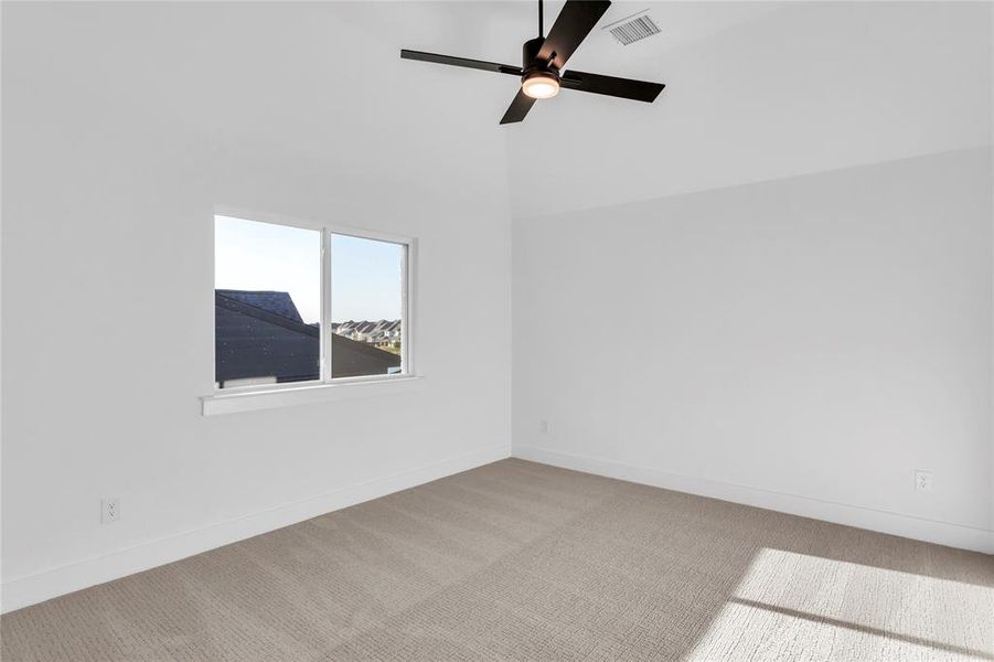Carpeted empty room featuring a ceiling fan and vaulted ceiling