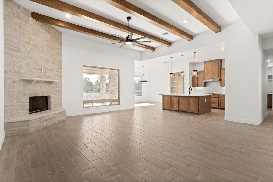 Unfurnished living room with a stone fireplace, a ceiling fan, a chandelier, beam ceiling, and light wood-style flooring