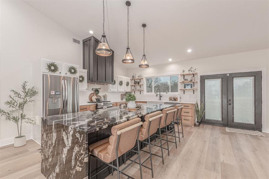 Kitchen with dark stone countertops, a kitchen breakfast bar, stainless steel appliances, a center island, and hanging light fixtures