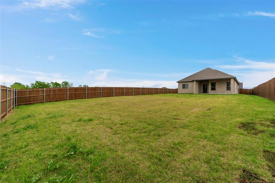 Expansive fenced backyard with a single-story brick exterior home