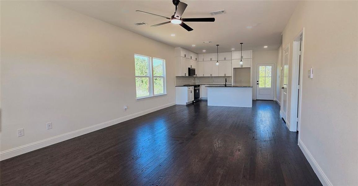 Unfurnished living room with a ceiling fan, dark wood finished floors, and healthy amount of natural light Unfurnished living room with a ceiling fan, dark wood finished floors, and healthy amount of natural light