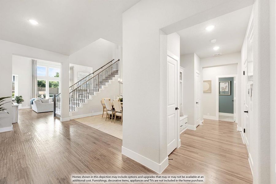 Open foyer with hardwood floors, staircase with iron railing, and hallway leading to dining area