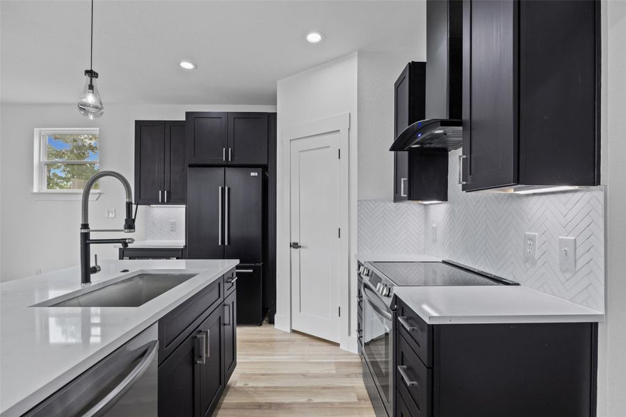 Modern kitchen featuring black cabinetry with brushed nickel hardware, white countertops, stainless steel appliances, and wood-finish flooring Modern kitchen featuring black cabinetry with brushed nickel hardware, white countertops, stainless steel appliances, and wood-finish flooring