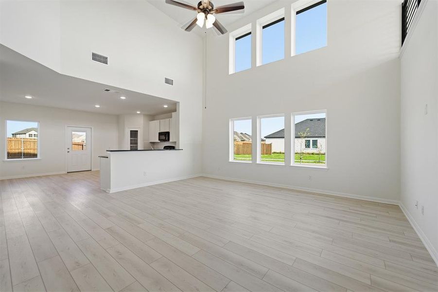 Spacious living area featuring a vaulted ceiling with a ceiling fan, light wood-finish flooring, and multiple large windows