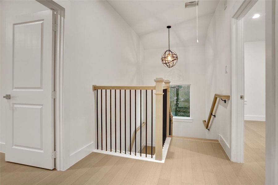 Bright upstairs landing with modern railing and stylish pendant lighting cohesive with downstairs lighting fixture.