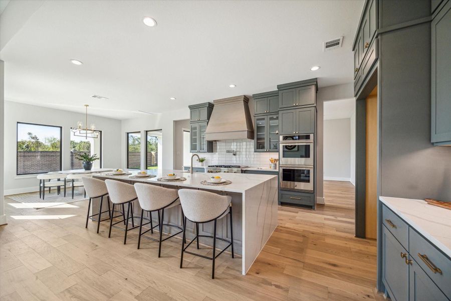 Chef's Kitchen with ceiling-high cabinets, high-end Jennair appliances, and massive island with waterfall countertop. Breakfast/Informal Dining Area off of Kitchen