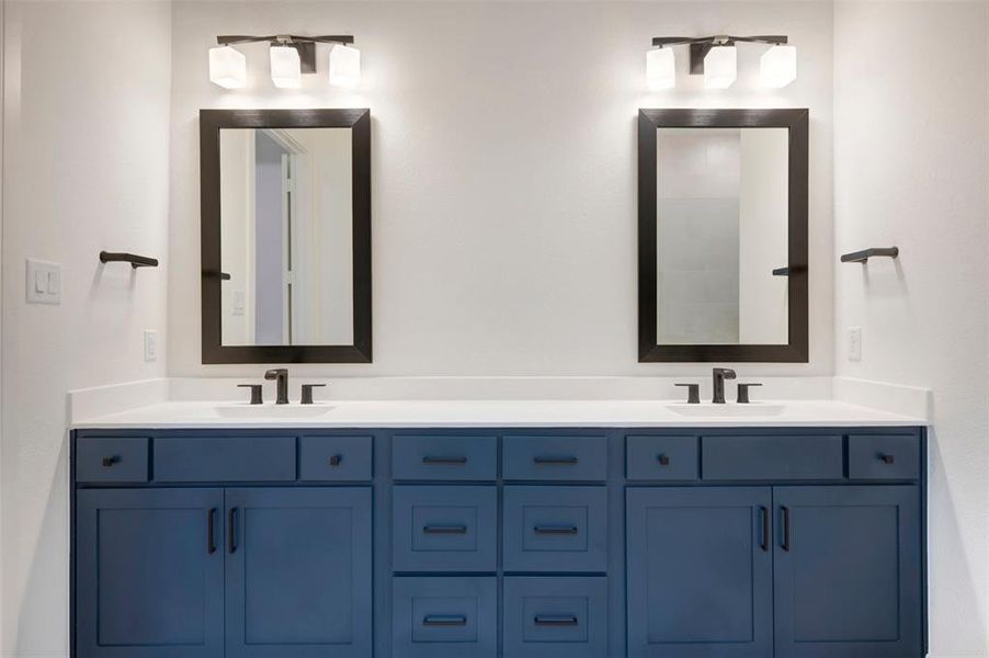 Bathroom featuring a dual vanity with navy blue cabinetry, white countertops, and contemporary black framed mirrors