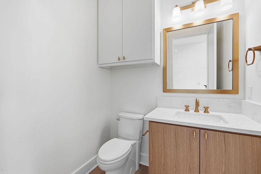 A modern vanity with wood cabinetry and stone counters anchors this powder room.