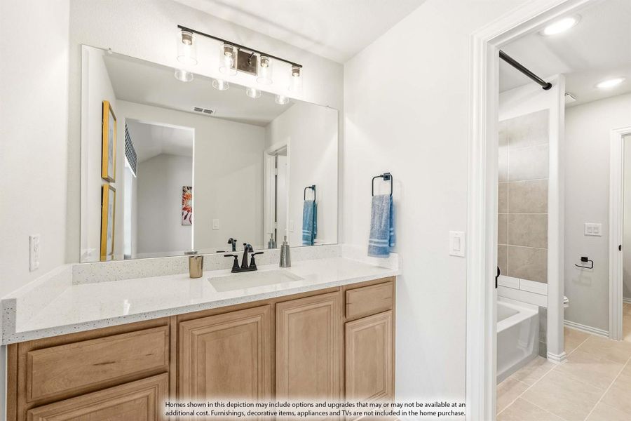 Bathroom with double sink vanity, wood cabinets, quartz countertop, large mirror, and tiled tub-shower combo visible in background.
