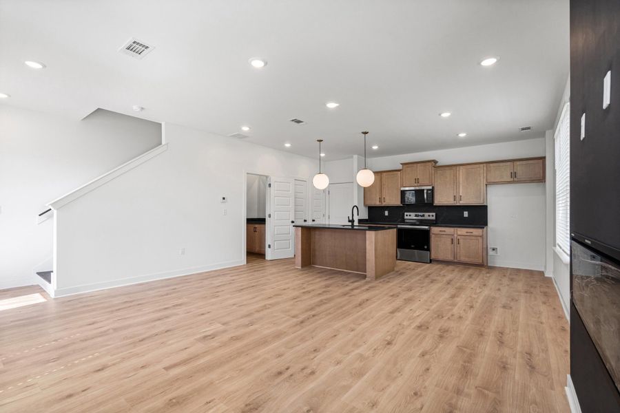 Open-concept living space featuring wood-finish flooring, recessed lighting, and a modern kitchen with a center island and stainless steel appliances
