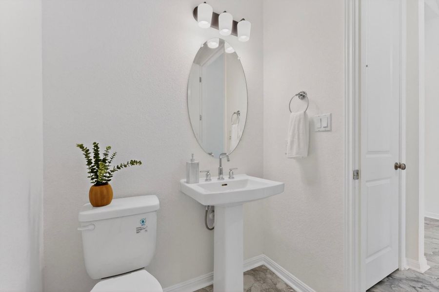 Pedestal sink with chrome fixtures, oval wall-mounted mirror, and three-light vanity fixture
