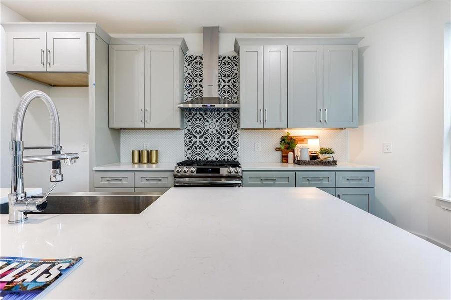 Kitchen with gray cabinets, sink, decorative backsplash, stainless steel range, and wall chimney exhaust hood