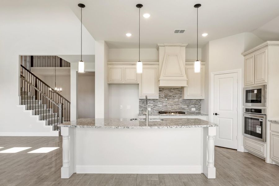 Kitchen with large island, granite countertops, white cabinets, tile backsplash, and pendant lights, open to staircase area. Kitchen with large island, granite countertops, white cabinets, tile backsplash, and pendant lights, open to staircase area.