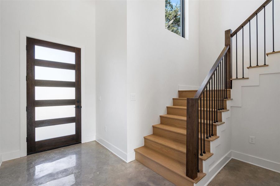 Entryway with finished concrete flooring, stairs, and a towering ceiling Entryway with finished concrete flooring, stairs, and a towering ceiling